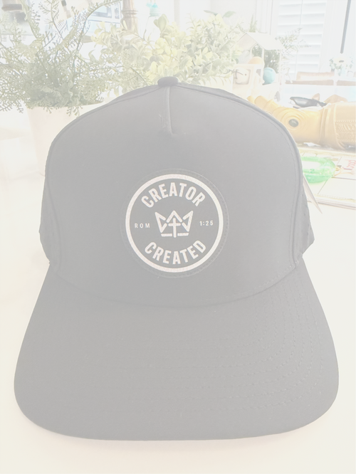 Black hat with 'Creator Over Created' logo on a blurred outdoor background